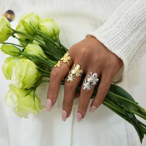 Gros plan de bagues papillon de luxe dorées et argentées sur les mains avec des fleurs