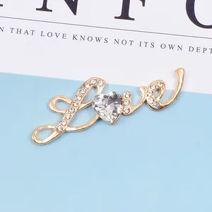 Detail der goldenen Love-Brosche mit herzförmigem Kristall und glitzernden Strasssteinen