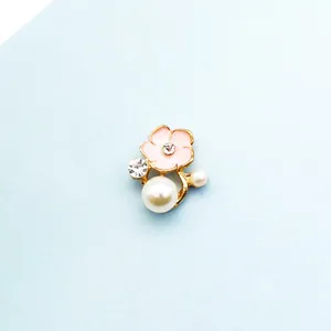 Makro-Detail von rosa Emaille-Blumen-Accessoire mit weißen Perlen und goldener Basis