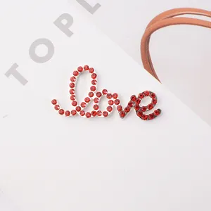 Macro shot of silver alloy Love script pendant with handset red rhinestones on white background