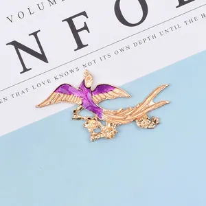 Detail of bird-shaped gold alloy charm with purple enamel wings and flower accents