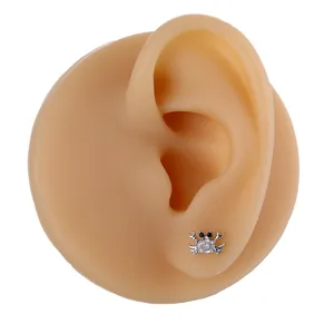 Macro detail of a silver crab stud earring with a clear zircon on a silicone ear model