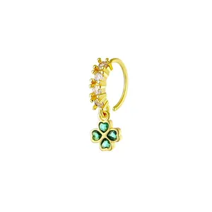 Detail of a C-shaped gold nose ring featuring white zircons and a green clover pendant