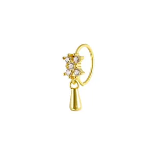 Macro view of gold nose ring with a zircon cross detail and dangling teardrop pendant