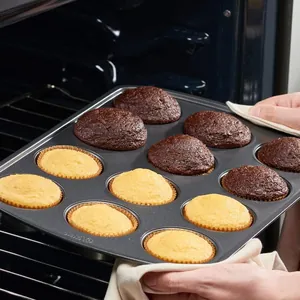 Baker holding 12-cup non-stick carbon steel muffin pan with fresh cupcakes