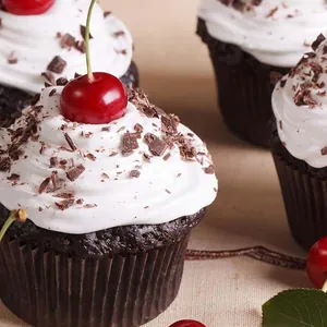 Cupcake de chocolate en molde de papel con crema blanca y cereza fresca encima
