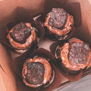 Primer plano de cuatro brownies de chocolate en moldes de tulipa marrón en caja kraft