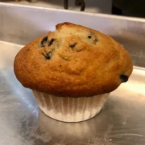 Close-up of a muffin with blueberry toppings in a white pleated paper liner on a metal tray