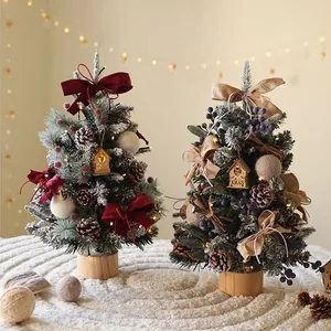 Miniature flocked desktop Christmas trees with glowing wood houses and pine cones