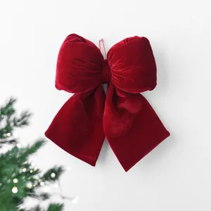 Deep red velvet Christmas bow ornament hanging on wall with festive pine branch