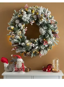 Close-up of snowy Christmas wreath with warm LED lights, pine cones and red berries