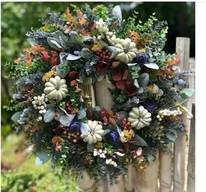 Kunstmatige herfstkrans met witte pompoenen en zijden bloemen aan een houten hek buiten hangend