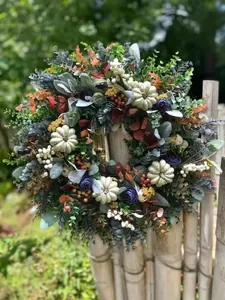 Detail van een herfstkrans met crème pompoenen en eucalyptus aan een houten hek