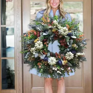 Herfstkrans met eucalyptus, pompoenen en bessen aan een houten voordeur opgehangen
