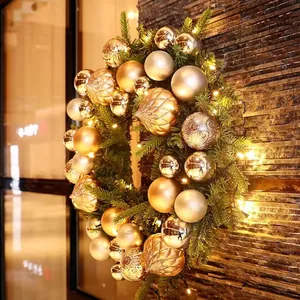 Detail of 40cm Christmas wreath with gold ornaments and warm LED lights on stone wall