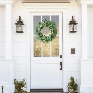 Close-up of artificial eucalyptus wreath on a white front door with black wall lamps