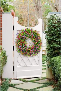 Detalle de una corona de flores artificiales colorida en una puerta de jardín blanca