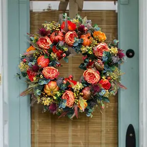 Detail eines Herbstkranzes mit orangefarbenen Rosen, Kürbissen und Laub an einer Tür
