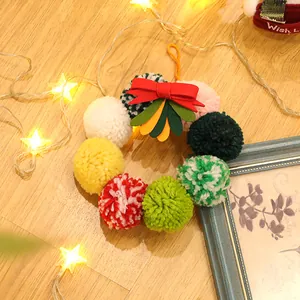 Detalle de corona de Navidad con pompones de colores, lazo rojo y luces LED cálidas