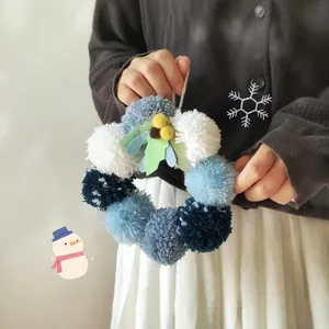 Corona navideña artesanal con pompones azules y blancos para decoración festiva