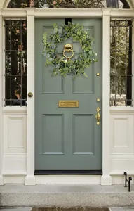 Close-up of eucalyptus wreath with white flowers hanging on a rustic green door