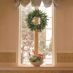 Artificial olive leaf wreath with green foliage and dark berries hanging on a window