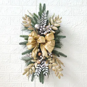 Detailed view of teardrop Christmas swag with gold bows and ornaments on white wall