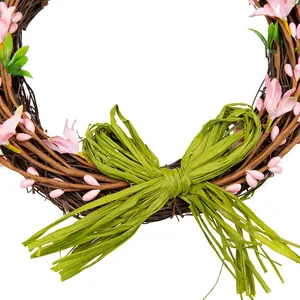 Détail d'une couronne de vigne artisanale avec fleurs roses et un grand nœud en raphia