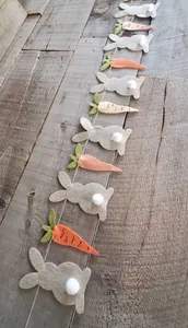 Détail de guirlande de Pâques en feutre avec lapins et carottes sur fond de bois
