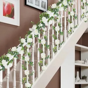 Detail of faux white roses and eucalyptus vine draped over a white staircase railing