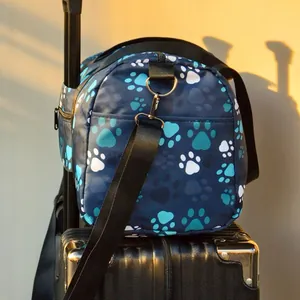 Dettaglio borsa da viaggio con impronte di zampe fissata al manico di una valigia nera
