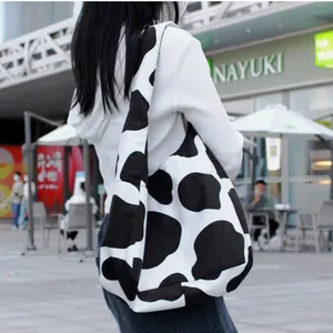 Bolso hobo de lona con estampado de vaca en blanco y negro y correa ancha llevado por modelo