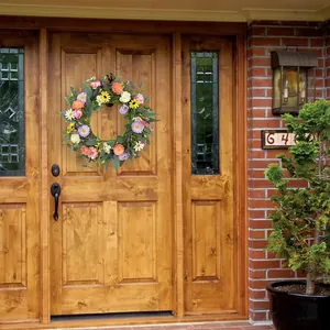 Couronne de marguerites sauvages aux fleurs colorées suspendue sur une porte en bois