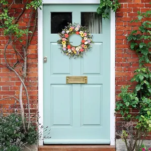 Détail d'une couronne de marguerites et roses artificielles sur une porte en bois bleu