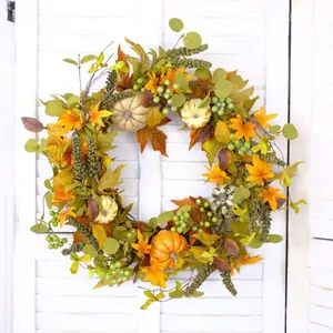 Fall wreath with maple leaves, pumpkins and green berries on white wooden shutter