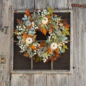 Detailed view of autumn wreath with white pumpkins and maple leaves on a rustic wooden door