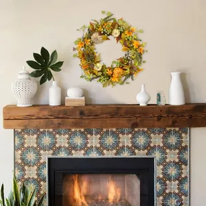 Fall wreath with pumpkins and maple leaves hanging above a cozy warm fireplace