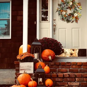 Autumn wreath with white pumpkins and maple leaves displayed on a cream front door