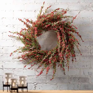 Corona de Navidad artificial con bayas rojas y piñas sobre una pared de ladrillo blanco