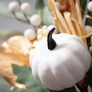 Macro di una zucca decorativa bianca con foglie dorate e bacche per decorazioni autunnali