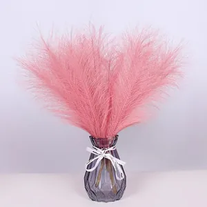 Pink artificial pampas grass in a purple faceted glass vase with a white decorative ribbon