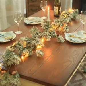 Snowy Christmas pine garland with warm LED lights and pinecones on a dining table