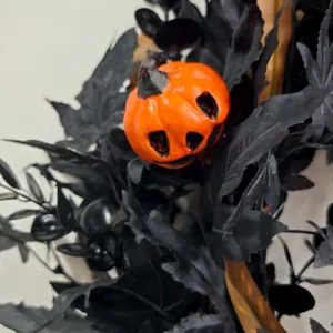 Close-up of Halloween wreath featuring an orange pumpkin and black maple leaves