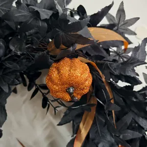 Close-up of Halloween wreath with black maple leaves and glitter orange mini pumpkins