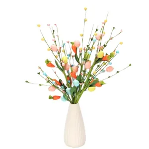 Tiges de Pâques avec des œufs colorés et des carottes dans un vase en céramique blanc