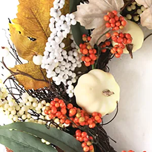 Detailed close-up of white pumpkins and orange berries on autumn maple leaf wreath
