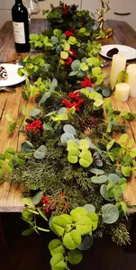Close-up of artificial red berry garland with pine needles on dark wood table