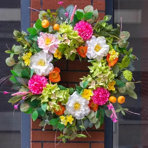 Colorful wildflower wreath with faux peonies and oranges hanging on a brick pillar