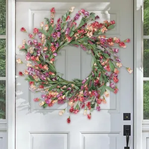 Front view of a vibrant artificial wildflower wreath with daisies on a gray wooden door