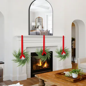 Set of three Norfolk pine Christmas wreaths with red satin ribbons on a white fireplace